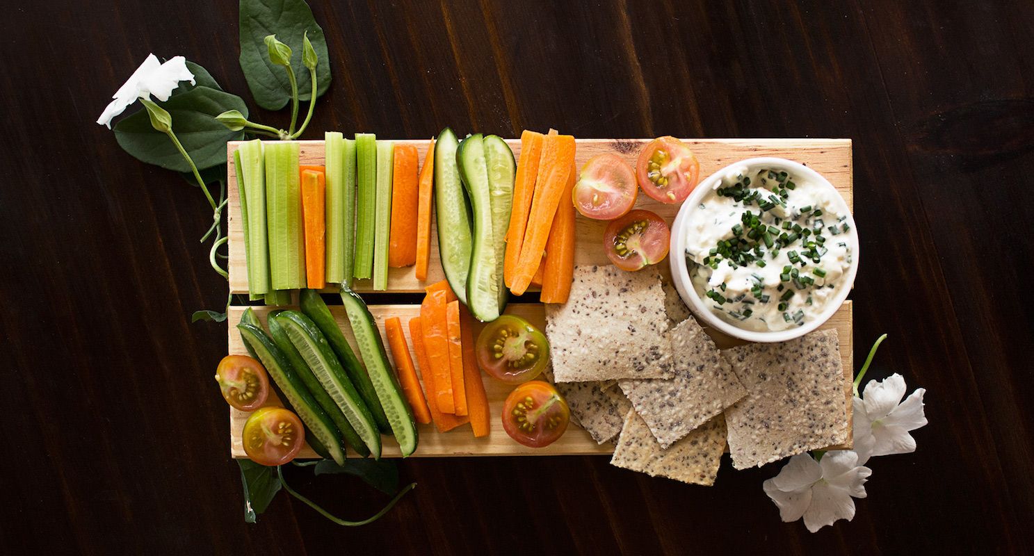 Galletas en una tabla junto a vegetales y un recipiente para acompañamiento